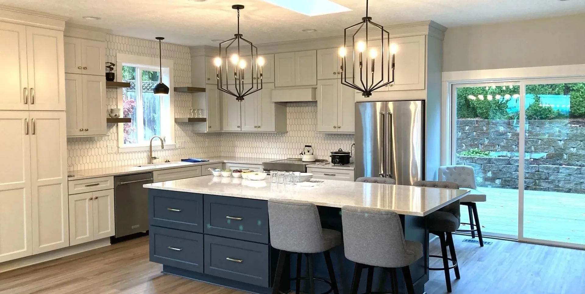 Custom kitchen remodel with large island seating, white cabinetry, hex tile backsplash, and pendant lighting.